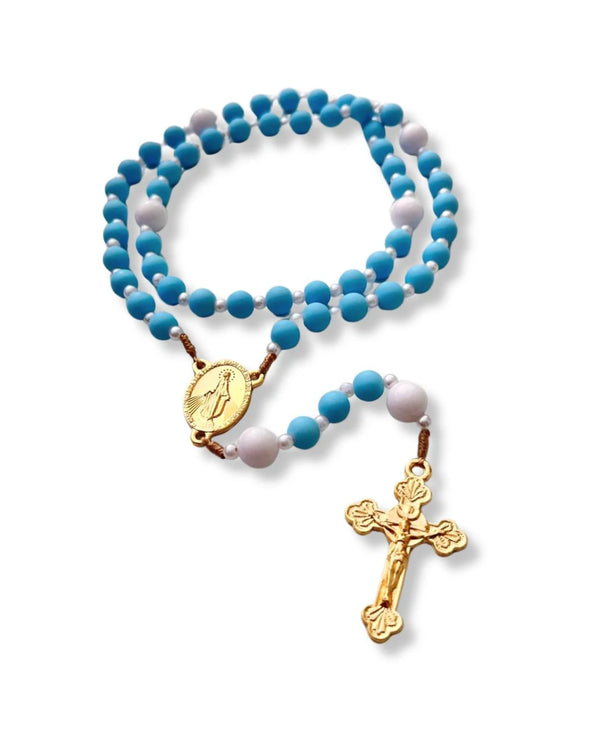 Terço de Nossa Senhora das Graças com contas emborrachadas azul-turquesa e brancas, intercaladas por pequenas pérolas, medalha dourada e crucifixo clássico. Produto enrolado sobre fundo branco.