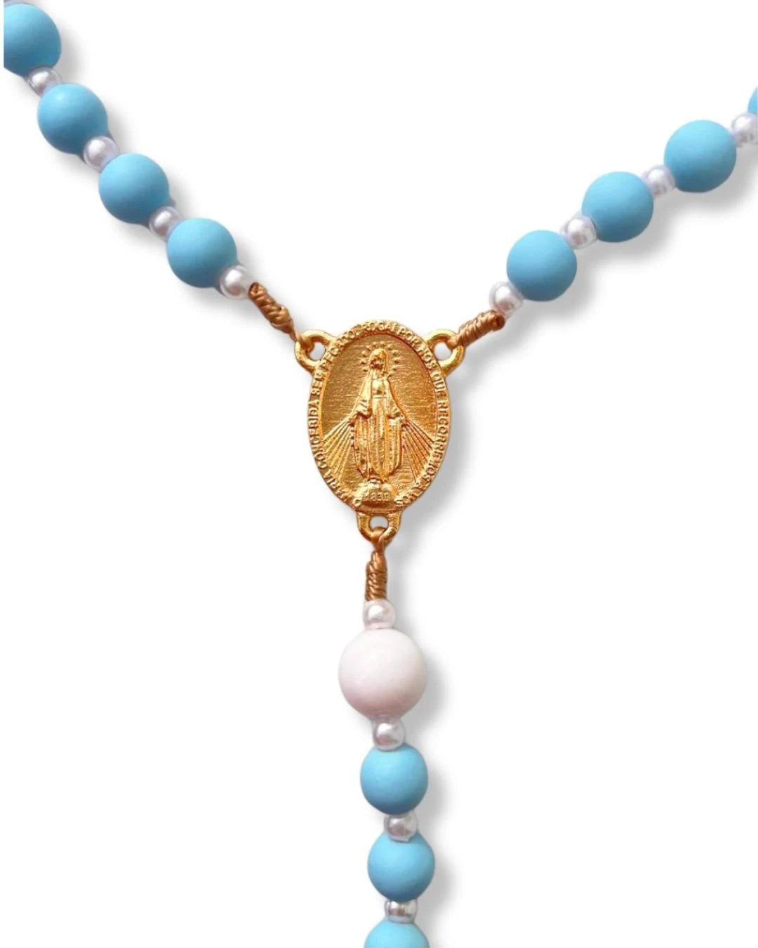 Detalhe ampliado da medalha dourada de Nossa Senhora das Graças no terço católico com contas azuis e brancas. Medalha com gravação em alto relevo.