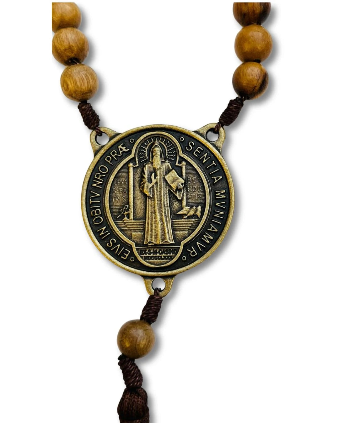 Vista frontal da medalha de São Bento em metal envelhecido, com representação do santo segurando a cruz e a Regra de São Bento. Inscrição em latim que invoca proteção contra o mal. 