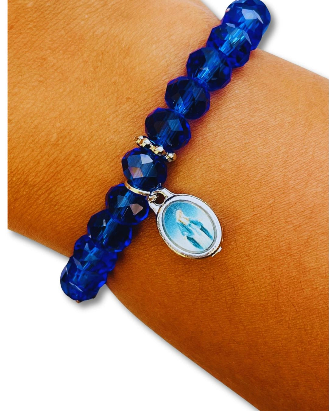 Pulseira de cristal azul com medalha de Nossa Senhora das Graças no pulso. Destaque para as contas facetadas que refletem a luz com intensidade.